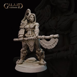 May include: A detailed figurine of a female orc warrior, holding a large axe. The orc is clad in armor and fur accents, with pointed ears and a determined expression. The base is a light tan color, and the logo "GALAAD" is at the top.