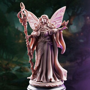 May include: A light-coloured, detailed figurine of a fairy-like figure with large, intricate wings, wearing a long, flowing robe with ornate patterns. The figure holds a tall, twisted staff in one hand and a small butterfly in the other hand.