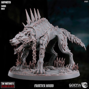 May include: A grey, detailed miniature of a wolf-like creature with a spiked collar and chain. The creature is standing on a round base with a textured surface. The miniature is labelled "Frontier Hound" and is part of the "The Butcher's Dominion" collection.