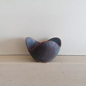 Könnte beinhalten: Eine kleine, abgerundete Keramikschale mit einem wellenförmigen, vierzackigen Rand. Die Außenseite hat eine tiefdunkle violette Grundfarbe mit einer gesprenkelten, strukturierten Oberfläche, während das Innere und der Rand in ein leuchtendes Blau übergehen.
