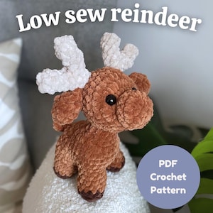 Könnte beinhalten: Ein braunes gehäkeltes Rentier mit weißen Geweihen und schwarzen Augen. Der Text "Low sew reindeer" steht über dem Rentier, und ein blauer Kreis mit "PDF Crochet Pattern" darunter. Das Rentier sitzt auf einer weißen Oberfläche.