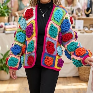 May include: A long-sleeved crochet cardigan featuring a vibrant patchwork of square panels. Each panel is adorned with a three-dimensional floral rose motif in bright shades of red, orange, blue, purple, and teal, finished with a hot pink trim.