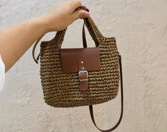 May include: A brown woven straw handbag with a brown leather flap and buckle closure. The bag has a long brown leather strap.