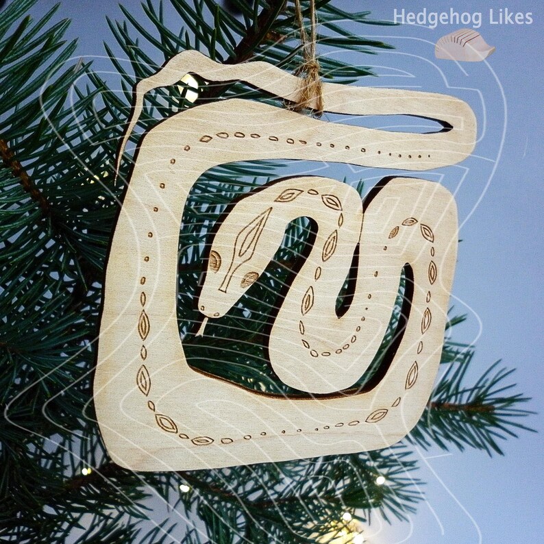May include: A wooden Christmas ornament shaped like a snake with a detailed design. The ornament is light brown and has a natural wood finish.