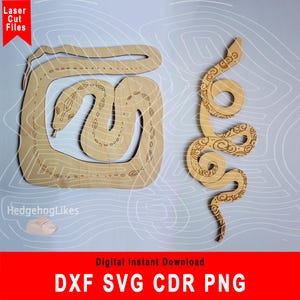 May include: Two laser cut wooden snake designs. One snake is curled in a square shape, the other is a more traditional snake shape. Both snakes have intricate patterns.