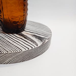 May include: A round wooden cake stand with a white and black wood grain pattern. The stand is made of wood and has a smooth, polished finish.