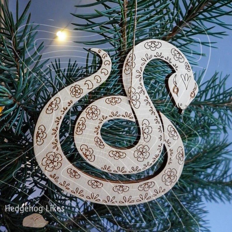 May include: A wooden snake ornament with a floral pattern, hanging on a Christmas tree. The snake is curled up in a circle, with its head facing the right side of the image.