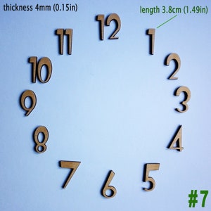 Può includere: Numeri di orologio in legno di colore marrone, da 1 a 12, su uno sfondo blu chiaro. I numeri sono lunghi 3,8 cm (1,49 pollici) e spessi 4 mm (0,15 pollici). I numeri sono disposti in cerchio, con il numero 12 in alto e il numero 1 a destra. Il testo "#7" si trova nell'angolo in basso a destra.