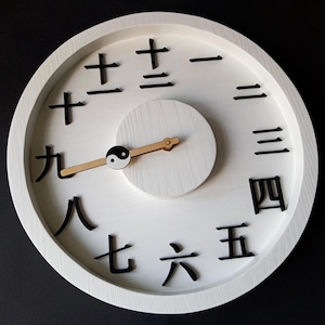 Peut inclure: Horloge murale en bois blanc avec des chiffres chinois noirs indiquant les heures. Le cadran de l'horloge comporte un petit cercle blanc avec un symbole yin-yang et des aiguilles en bois. Design simple et moderne.