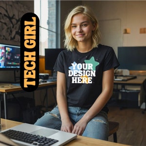 May include: A woman wearing a black t-shirt with the text "YOUR DESIGN HERE" and colorful star designs. She is sitting at a desk with a laptop in front of her.
