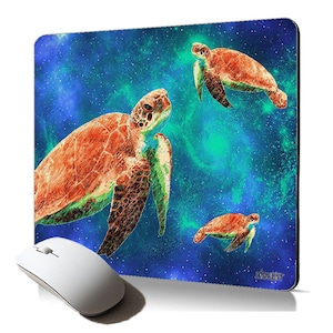 Op de afbeelding: Een muismat met een blauwe en groene galaxie achtergrond met drie zeeschildpadden. De schildpadden zijn oranje en bruin met groene accenten. De grootste schildpad is op de voorgrond en de kleinste schildpad is op de achtergrond.