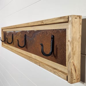 May include: Rustic wooden coat rack with a metal back panel featuring a rusty finish. The rack has four black metal hooks.