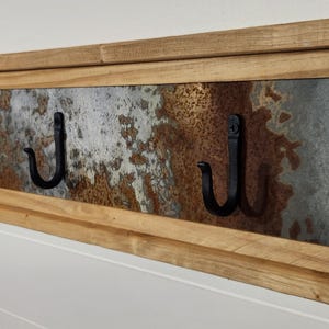 May include: Rustic wooden wall mounted coat rack with three black metal hooks. The rack has a distressed metal panel with a rusty and weathered look.