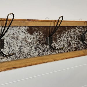 May include: A wooden coat rack with a cowhide pattern and four metal hooks.