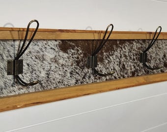 May include: A wooden coat rack with a cowhide pattern and four metal hooks.