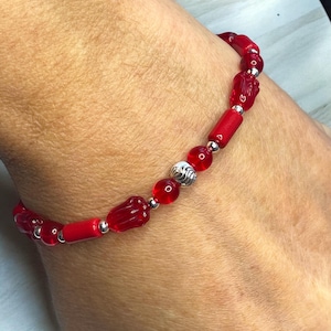 May include: Red glass bead bracelet with silver accents. The bracelet is made with red glass beads, some of which are shaped like hands, and silver spacer beads.