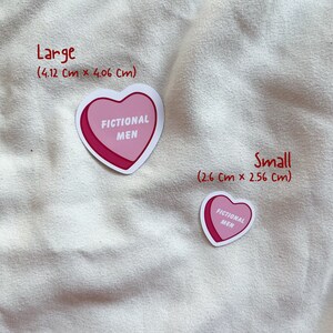 May include: Two heart-shaped stickers with the text "FICTIONAL MEN" in black lettering on a pink background. The larger sticker measures 4.12 inches by 4.06 inches, and the smaller sticker measures 2.6 inches by 2.56 inches.