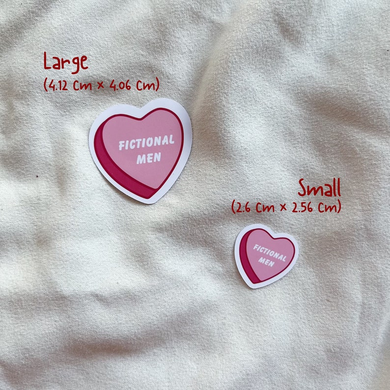 May include: Two heart-shaped stickers with the text "FICTIONAL MEN" in black lettering on a pink background. The larger sticker measures 4.12 inches by 4.06 inches, and the smaller sticker measures 2.6 inches by 2.56 inches.