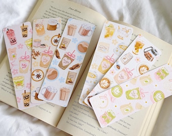 May include: A collection of colorful bookmarks featuring illustrations of various beverages, including coffee, tea, and bubble tea. The bookmarks are placed on an open book with text visible. The designs include pink, brown, and green accents.