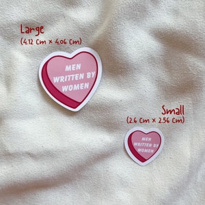 May include: Two pink heart-shaped stickers with the text "MEN WRITTEN BY WOMEN" in white. The larger sticker measures 4.12 cm by 4.06 cm and the smaller sticker measures 2.6 cm by 2.56 cm.