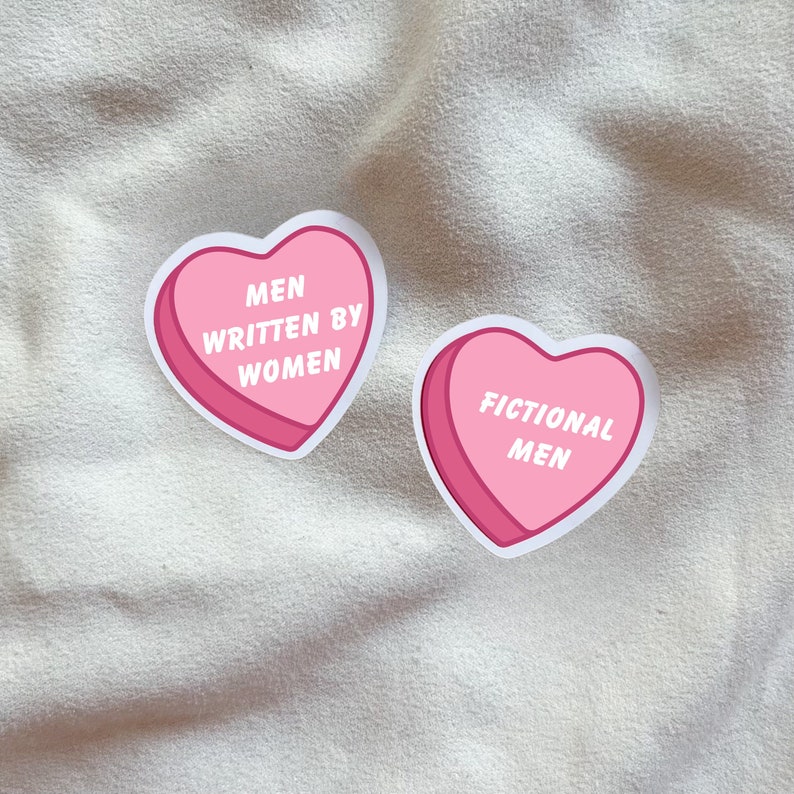 May include: Two pink heart-shaped stickers with white outlines. The left sticker says "Men Written By Women". The right sticker says "Fictional Men".