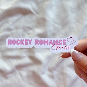 Könnte beinhalten: Ein weißer Aufkleber mit rosa Schriftzug, der "Hockey Romance Girlie" mit zwei rosa Herzen lautet.