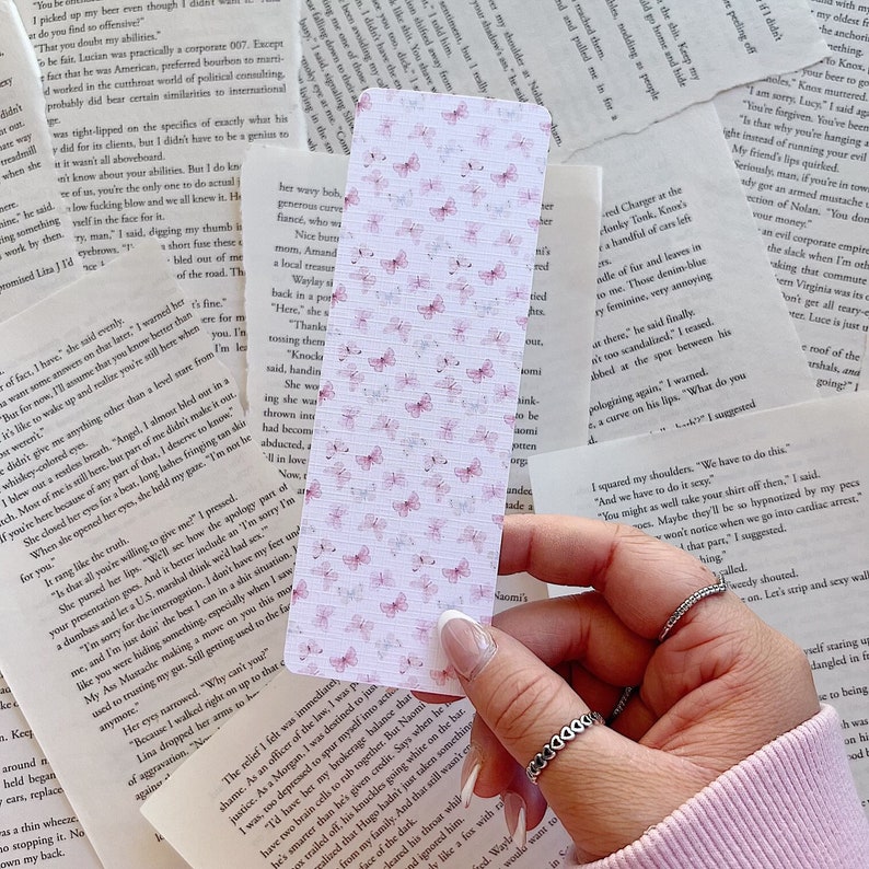Op de afbeelding: Een witte bladwijzer met een delicaat patroon van roze vlinders. De bladwijzer is gemaakt van papier en heeft een licht getextureerd oppervlak.