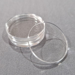 Könnte beinhalten: Ein Stapel runder, transparenter Acrylscheiben, wobei eine Scheibe auf dem Stapel liegt.