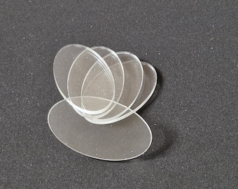 May include: A collection of clear, oval-shaped acrylic pieces arranged in a layered pattern. The transparent elements are set against a dark background, creating a contrast that highlights their form. The pieces appear to be smooth and reflective.