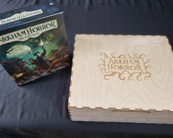 May include: A wooden box and a game box for "Arkham Horror: The Card Game." The game box features a colorful illustration of a man with a lantern, monsters, and the text "Arkham Horror The Card Game." The wooden box has the game's logo.