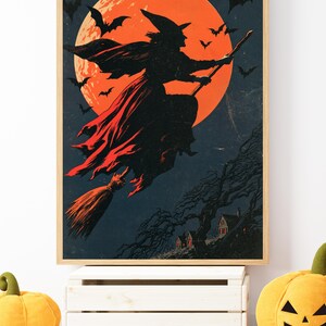 K&ouml;nnte beinhalten: Ein gerahmter Kunstdruck mit der Silhouette einer Hexe, die auf einem Besen vor einem gro&szlig;en, leuchtend orangefarbenen Vollmond fliegt. Der dunkle Nachthimmel ist voller fliegender Flederm&auml;use und ein kleines Haus steht zwischen kahlen B&auml;umen.