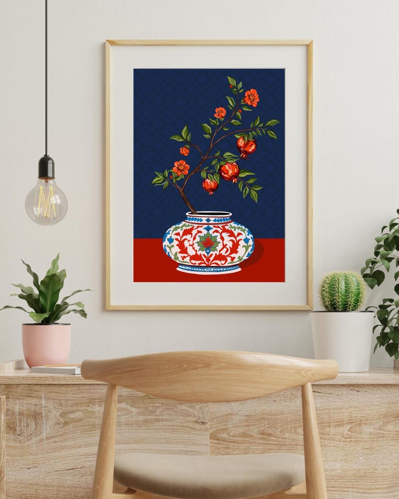 May include: A framed wall art print featuring a decorative ceramic vase with a white base, red floral patterns, and blue accents. A branch with green leaves, orange flowers, and red pomegranate fruits emerges from the vase against a dark blue background.