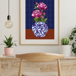 May include: A framed wall art print featuring a white vase with blue and red floral patterns containing vibrant pink peony flowers. The background consists of a dark blue patterned wall section above a solid brown surface, all enclosed in a light wood frame.