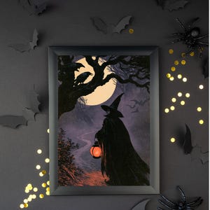 Peut inclure: Un cadre rectangulaire noir contenant une impression repr&eacute;sentant une silhouette v&ecirc;tue d'une cape sombre et d'un chapeau pointu marchant sur un chemin nocturne. La silhouette tient une lanterne orange sous une pleine lune avec des corbeaux.