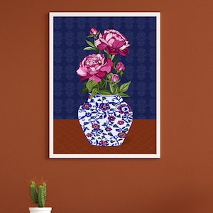 May include: A framed wall art print featuring a white and blue porcelain vase decorated with small red and blue floral patterns. The vase holds a bouquet of vibrant magenta peonies with green leaves, set against a dark blue background with a subtle pattern.