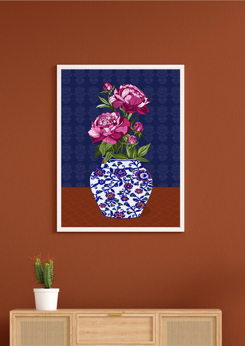 May include: A framed wall art print featuring a white and blue porcelain vase decorated with small red and blue floral patterns. The vase holds a bouquet of vibrant magenta peonies with green leaves, set against a dark blue background with a subtle pattern.