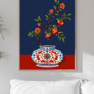 May include: A framed wall art print featuring a pomegranate branch with orange-red flowers and ripe red fruits emerging from a white, red, and blue patterned ceramic vase. The background is a deep navy blue with a subtle repeating floral pattern.