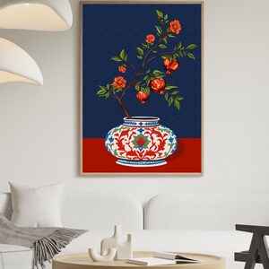 May include: A framed wall art print featuring a decorative white ceramic vase with intricate red and blue floral patterns. A branch with green leaves, orange blossoms, and red pomegranate fruits emerges from the vase against a dark blue background.