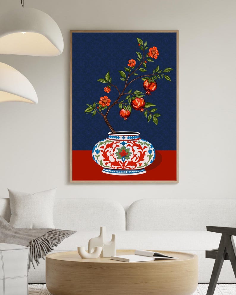 May include: A framed wall art print featuring a decorative white ceramic vase with intricate red and blue floral patterns. A branch with green leaves, orange blossoms, and red pomegranate fruits emerges from the vase against a dark blue background.