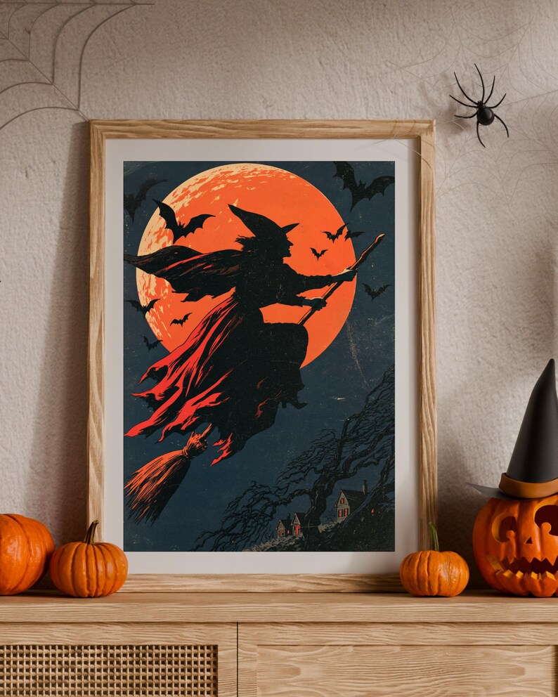 K&ouml;nnte beinhalten: Ein gerahmter Kunstdruck mit der Silhouette einer Hexe, die auf einem Besen vor einem gro&szlig;en, leuchtend orangefarbenen Vollmond fliegt. Der dunkelblaue Nachthimmel ist voller fliegender Flederm&auml;use und ein kleiner, dunkler, blattloser Baum steht &uuml;ber H&auml;usern.