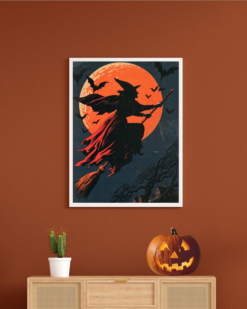 K&ouml;nnte beinhalten: Ein gerahmter Wandkunstdruck mit der Silhouette einer Hexe, die auf einem Besenstiel vor einem gro&szlig;en, leuchtend orangefarbenen Vollmond fliegt. Der dunkelblaue Nachthimmel ist voller fliegender Flederm&auml;use und ein dunkler, blattloser Baum steht &uuml;ber einem kleinen Haus.