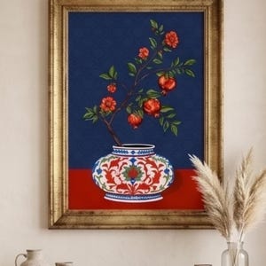 May include: A framed wall art print featuring a decorative vase with a red and white floral pattern. A branch with green leaves, red flowers, and pomegranates emerges from the vase against a dark blue background, set on a solid red surface.