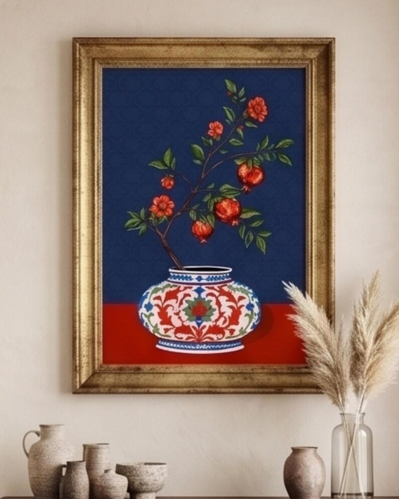 May include: A framed wall art print featuring a decorative vase with a red and white floral pattern. A branch with green leaves, red flowers, and pomegranates emerges from the vase against a dark blue background, set on a solid red surface.