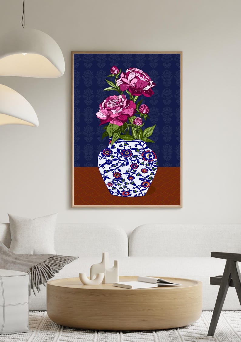 May include: A framed wall art print featuring a white and blue ceramic vase with a floral pattern, filled with vibrant pink peony flowers and green leaves. The background consists of a dark blue patterned wall and a solid brown surface.