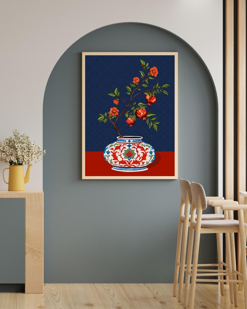 May include: A framed wall art print featuring a decorative white vase with intricate red and blue floral patterns. A branch with green leaves, orange blossoms, and red pomegranate fruits emerges from the vase against a dark blue background.
