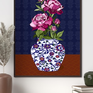 May include: A framed wall art print featuring a white vase with blue and orange floral patterns containing vibrant pink peony flowers and green leaves. The background consists of a dark blue wall with a subtle pattern and a brown surface below.