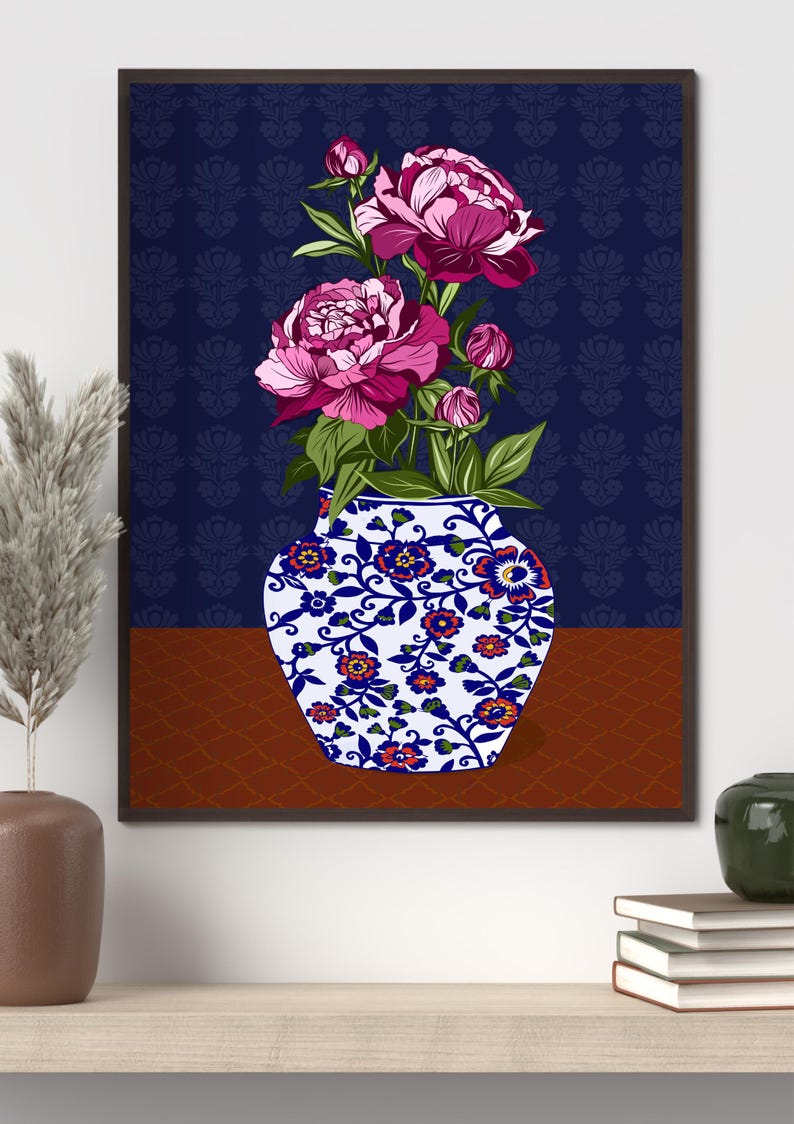 May include: A framed wall art print featuring a white vase with blue and orange floral patterns containing vibrant pink peony flowers and green leaves. The background consists of a dark blue wall with a subtle pattern and a brown surface below.