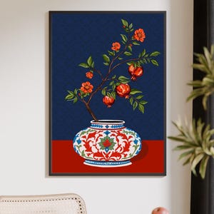 May include: A framed wall art print featuring a decorative white vase with intricate red and blue floral patterns. A branch with green leaves, orange blossoms, and red pomegranate fruits emerges from the vase against a dark blue background.