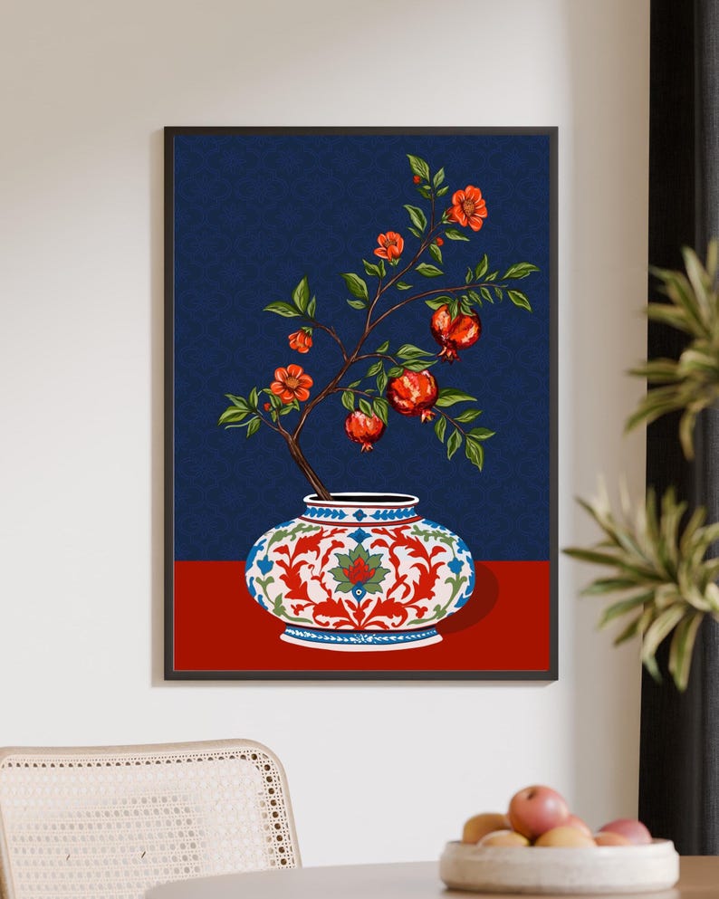 May include: A framed wall art print featuring a decorative white vase with intricate red and blue floral patterns. A branch with green leaves, orange blossoms, and red pomegranate fruits emerges from the vase against a dark blue background.