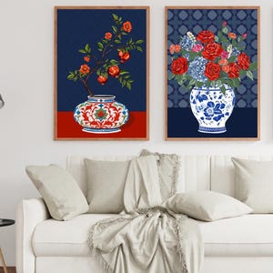 May include: Two framed wall art prints. The left print shows a pomegranate branch in a red and white patterned vase on a red surface. The right print features a bouquet of red roses and blue hydrangeas in a blue and white floral vase.